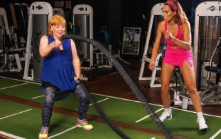 Woman over 40 performs battle rope exercise while female personal trainer encourages her